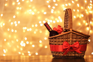 Gift basket with bottle of wine against blurred lights. Space for text