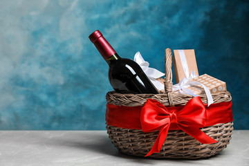Gift basket with bottle of wine on color background. Space for text