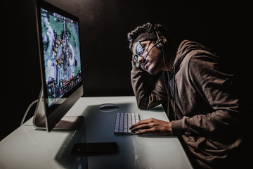 Technology, gaming, entertainment, let's play and people concept. Portrait of sad young man in headset with pc computer playing game at home and streaming playthrough or walkthrough video