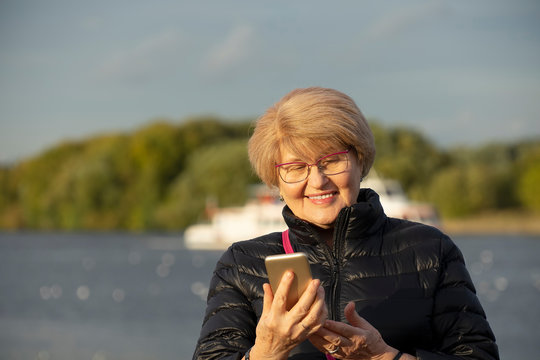 Senior woman walk in the park and look at smartphone