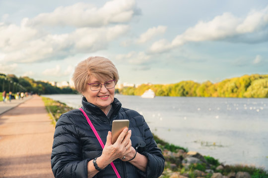 Senior woman walk in the park and look at smartphone