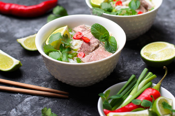 Traditional Vietnamese Soup Pho Bo with Rice Noodles, Beef and Herbs on Dark Background