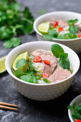 Traditional Vietnamese Soup Pho Bo with Rice Noodles, Beef and Herbs on Dark Background