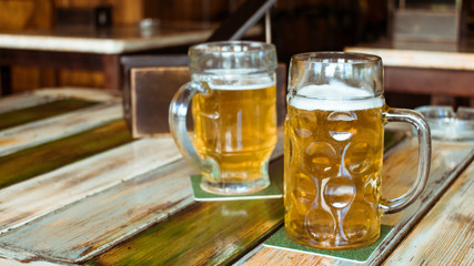 Glasses of light beer on pub background. Pint glass of golden beer with snacks and grill food on wooden table in pub, bar