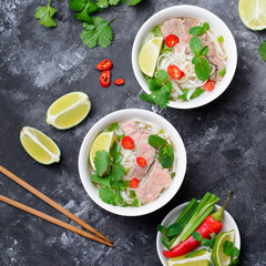 Traditional Vietnamese Soup Pho Bo with Rice Noodles, Beef and Herbs on Dark Background