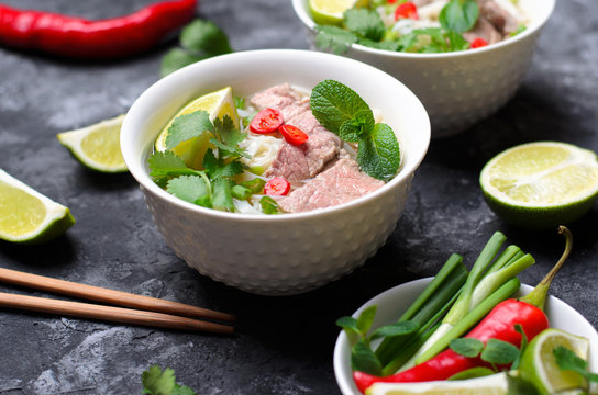 Traditional Vietnamese Soup Pho Bo with Rice Noodles, Beef and Herbs on Dark Background
