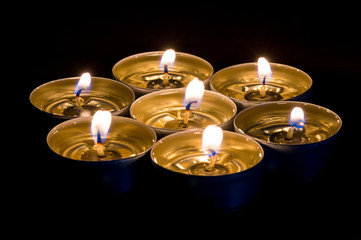 Small candles burning with black background. Candles with liquid wax.