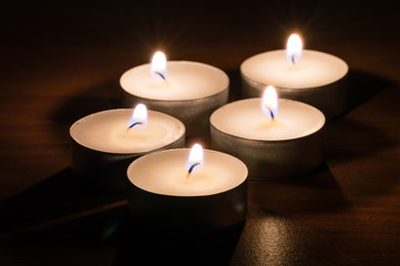 Small wax candles burning on wooden table at night.