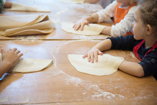 Hands of children rolling pizza dough on the kitchen table. Making pizza.