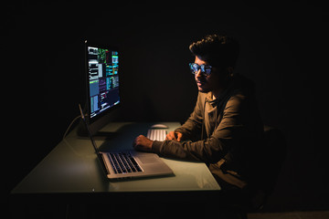Indian male programer in dark room writing code or using computer and laptop for virus program for...
