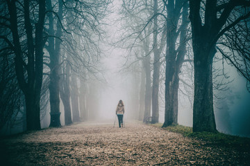 Alone woman and morning walk in misty park full of trees
