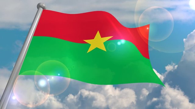 The flag of the state of Burkina Faso develops in the wind against a blue sky with cumulus clouds and a flash on the lens from the sun. 4K video is looped and decoded from a 3D program.