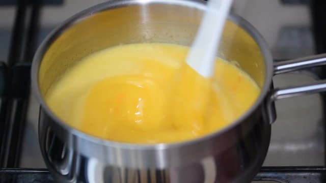 Cooking of orange curd in a saucepan.