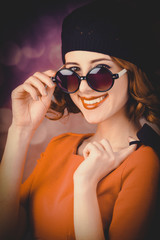 portrait of a beautiful girl with curly hair dressed in a beret and sunglasses against a gray background.