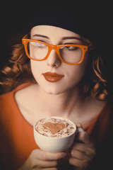 portrait of a beautiful girl with curly hair dressed in a beret and glasses holding a cup of coffee against a red background.