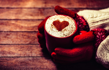 Hands in mittens holding hot cup of coffee. Photo with focus on heart.