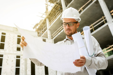 Construction engineer in a white hardhat inspecting blueprints on a construction site.