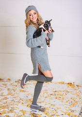 A beautiful young woman holding two puppies. Smiling blondie wearing grey dress with pets in her hands on white background.