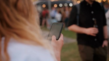 Behind shoulder conematic shot of woman use smartphone at foodtruck festival or hipster party. text and send message or photos through app. Concept connectivity and addiction to social media - Powered by Adobe