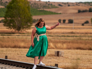 A blonde woman with a green dress walking on the train tracks in autumn