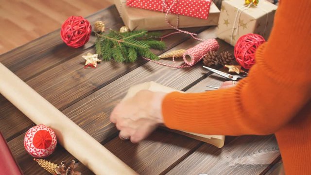 Christmas flat lay of unready hand crafted gift box on rustic wooden table with rolls of craft and colour wrapping paper, pine cones, fir branches and decor elements.