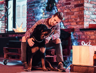 Young man sitting with his purebred rottweiler in a decorated living room at christmas time.