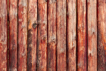 Wonderful texture of old wooden logs of an unusual moraine color. Wooden texture background. The sharp shade of a wooden fence made of logs, opened with a burgundy stain.