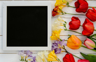 Tulips with blank black chalkboard picture frame on wooden background. 