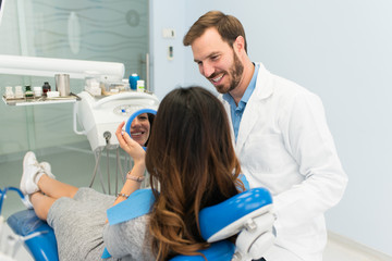 Happy smiling dentist showing female patient white teeth. Dentist repairing teeth in dental office. Teeth whitening procedure.