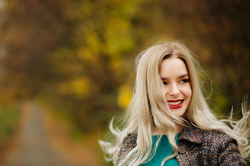 Positive blonde model in autumn coat posing near the yellow trees. Empty space