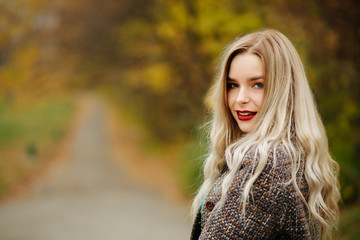 Naklejka premium Cheerful blonde model in autumn coat posing near the yellow trees. Empty space