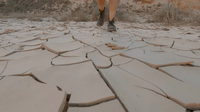Heavy duty brown leather boots or hiking shoes. Woman traveler walks on dry soil. Draught suffering land or earth in desert or river. Concept global warming and climate change effects