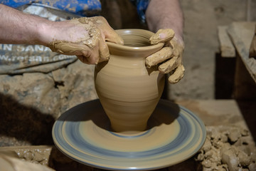 Fototapeta na wymiar hands of potter creating jar on a circle