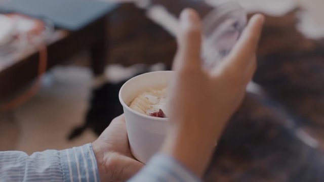 Young healthy yoga lifestyle woman, opens lid of take away organic treat or snack. Porrifdge with fresh fruits and chia seeds. Enjoys vegan breakfast at home or at work on the go