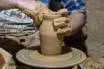 hands of potter creating a jar on circle
