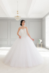 Fototapeta na wymiar Young brunette bride in white luxury wedding dress. Classic studio interior, full-lenght portrait
