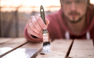 man paints with white paint on wooden planks