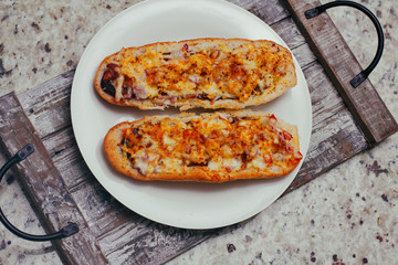 Two baguettes with cheese, ketchup and spice on white plate and wool tray background..