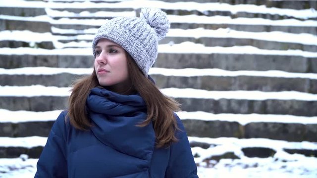 Close up Portrait of stylish young beautiful woman with a brooding look in a winter park over snowy background. Young beautiful model posing over winter forest. Stylish fashion portrait.