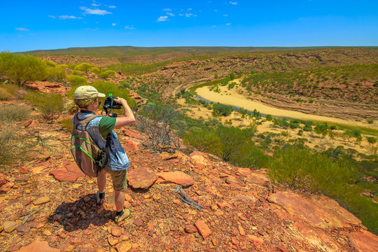 Travel photographer backpacker with stabilizer takes shot at Murchison River Gorge in Kalbarri National Park, Western Australia. Videomaker with professional camera takes photo in Australian outback.