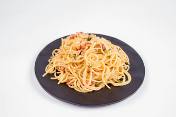 Spaghetti Carbonara with some parsley on a black plate on a white background