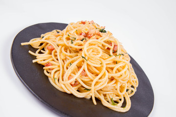 Spaghetti Carbonara with some parsley on a black plate on a white background