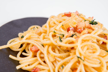 Spaghetti Carbonara with some parsley on a black plate on a white background