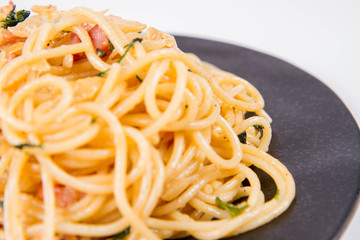 Spaghetti Carbonara with some parsley on a black plate on a white background
