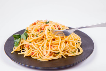 Spaghetti Carbonara with some parsley on a black plate on a white background being eaten with a fork
