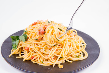 Spaghetti Carbonara with some parsley on a black plate on a white background being eaten with a fork