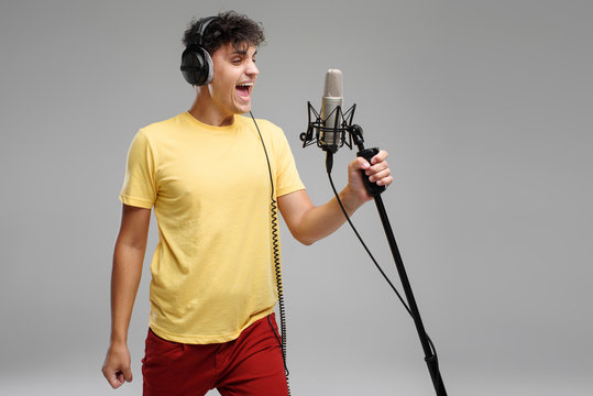 Portrait of handsome man in headphones sing on studio microphone on grey background. Singer concept.