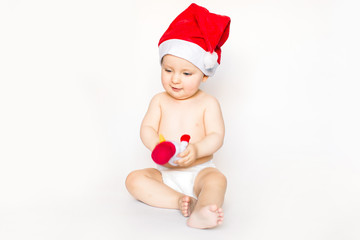 Christmas and family concept - cute funny baby in red santa hat sitting on white floor at home, humor, joke and holding a little snowman