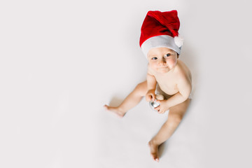 Adorable little girl is sitting on floor, wearing red Christmas cap, isolated on the white background