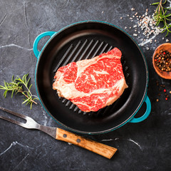 Raw Fresh Marbled Meat Beef Steak rosemary, spices on the grill pan. Black marble background. Top...